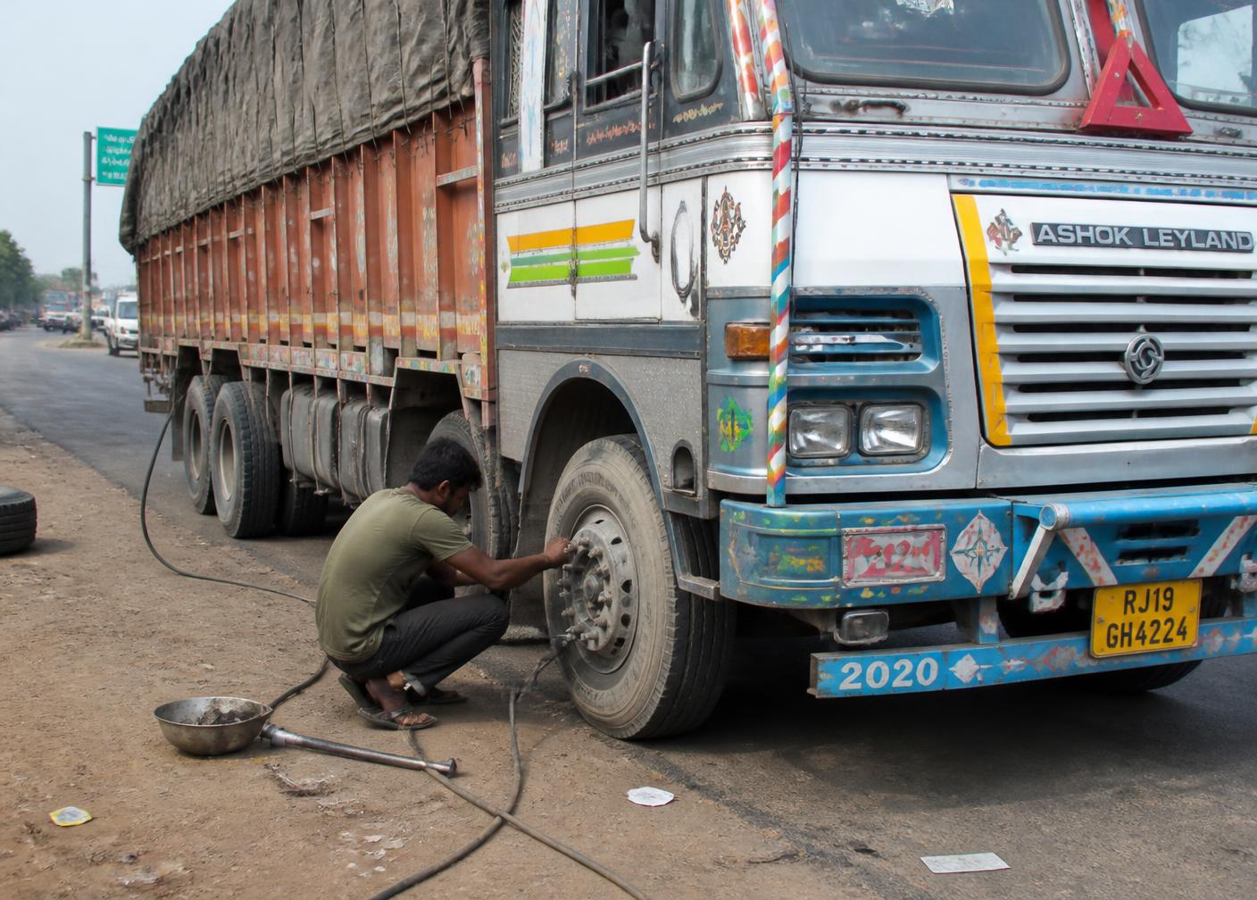 Tyre technician assisting a stopped vehicle on an Indian road